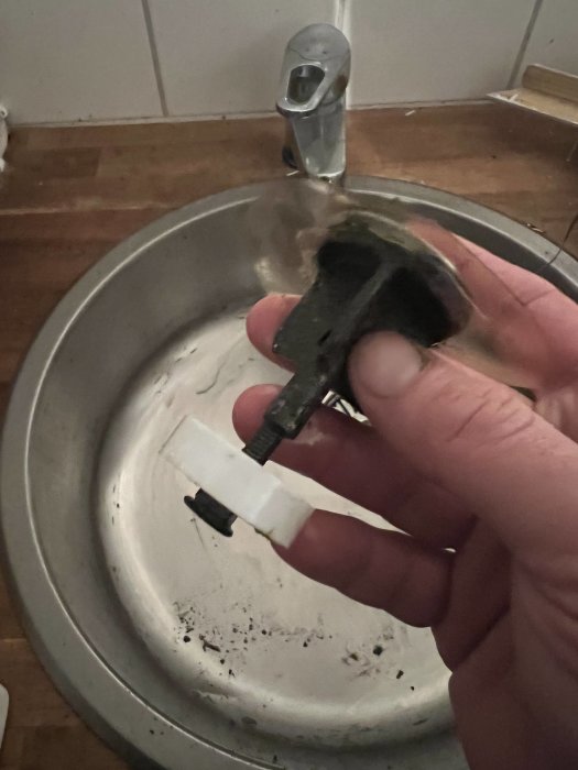 Hand håller en bränd elkontakt framför en tvättställsblandare.