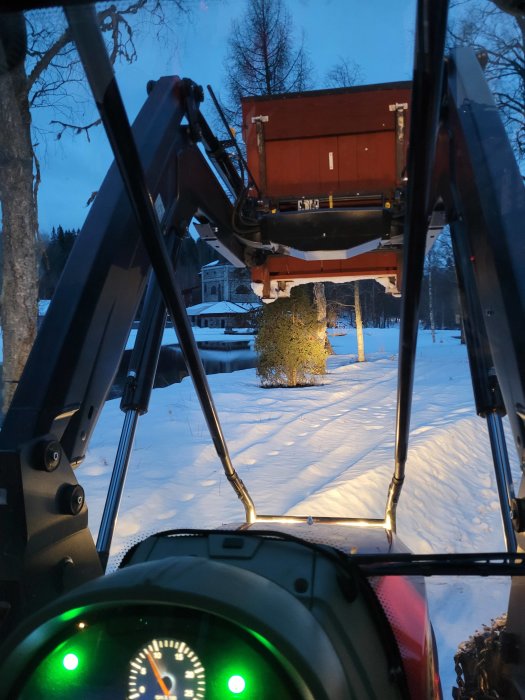 Vy från förarhytten på en traktor med en svetsad verktygslåda monterad på lastarfästen i vinterlandskap.