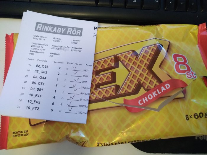 Faktura från Rinkaby Rör ovanpå en påse chokladkex vid tangentbord.