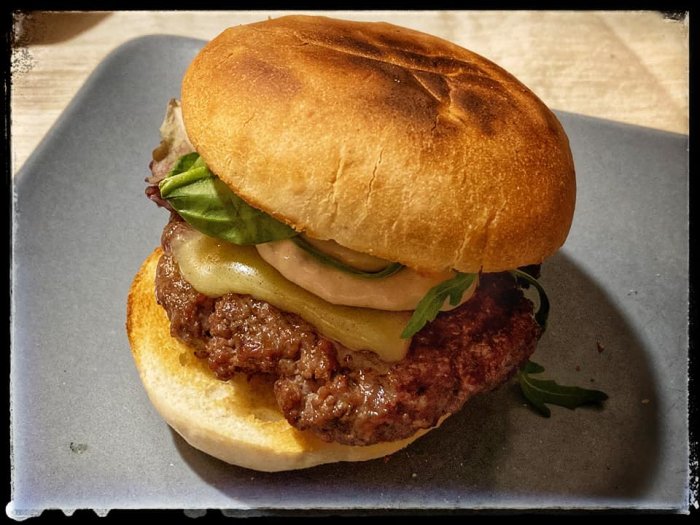 Juicy hamburgare med smält ost och gröna blad mellan rostade brödhalvor på en tallrik.