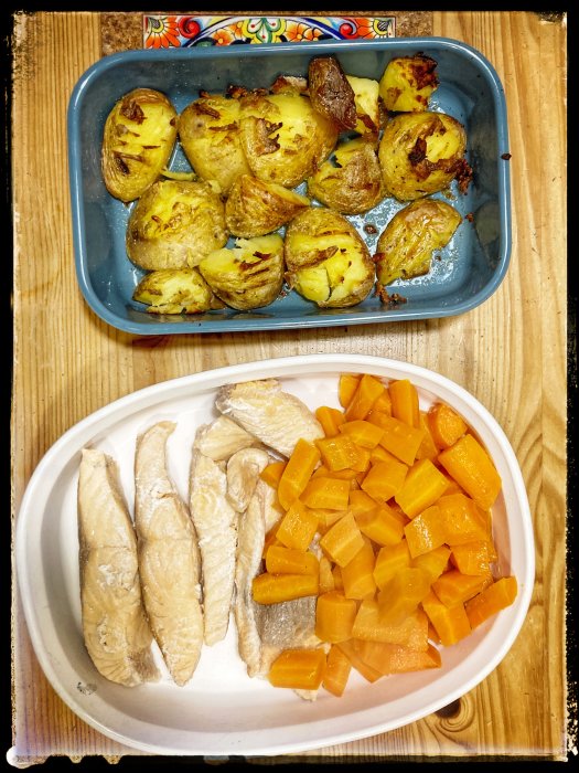 Kryddrostad potatis i ugnsform och kokt fisk med morotsbitar på vit tallrik.