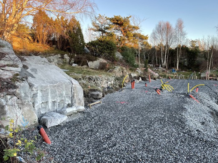 Byggarbetsplats förberedd för pålning med markerade punkter och grus, omgiven av berg och vegetation.