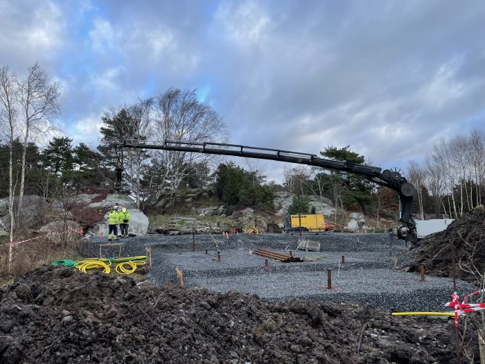 Grundläggningsarbete med maskinell pålning på en byggarbetsplats, arbetare synliga och markerade områden.