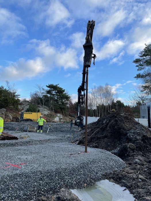 Bergborrningsrigg vid pålningsarbete, armeringsjärn och materialhögar på byggplats.