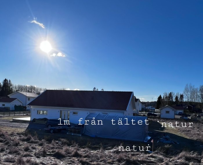 Ett hus med ett blått tält på sidan, mot bakgrund av ett öppet naturområde och solig himmel.