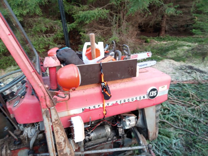 Verktyg och utrustning på en röd Massey Ferguson 135 traktor, med skog i bakgrunden.