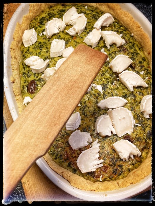 Ogräddad paj med getostbitar ovanpå ett lager av äggstanning, redo att gräddas i ugn.