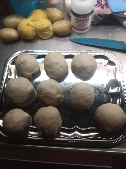 Degbollar på bakplåt med potatis, en citron och en handtvålsflaska i bakgrunden.