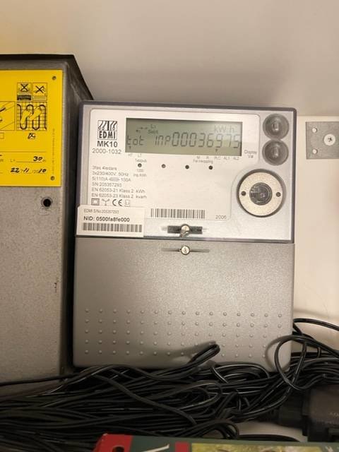Elmätare på vägg intill säkerhetscentral med synlig kWh-display och ledningar i förgrunden.