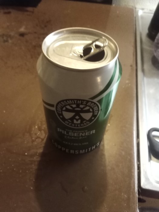 Aluminiumburk med öl märkt "Pilsener" på ett bord, delvis drucken med öppen flik.