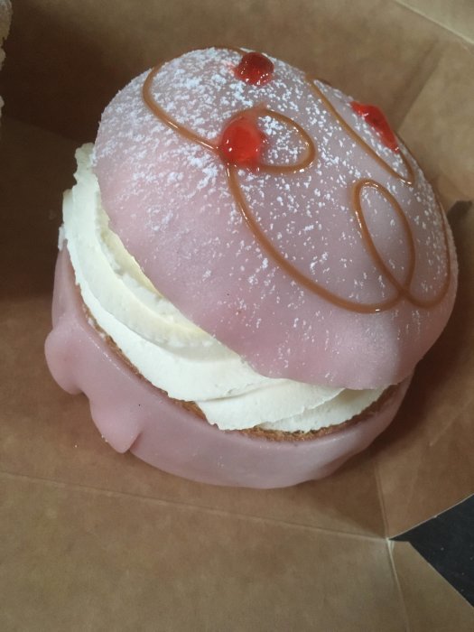 Halverad prinsessemla med rosa glasyr, grädde och gelédekoration, på brunt bakgrundspapper.