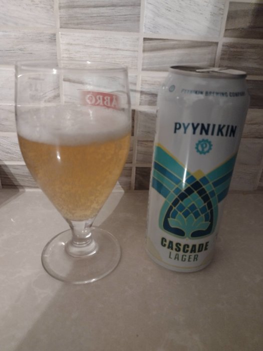 Glas med lageröl bredvid en Pyynikin Brewing Company Cascade Lager burk på köksbänk.