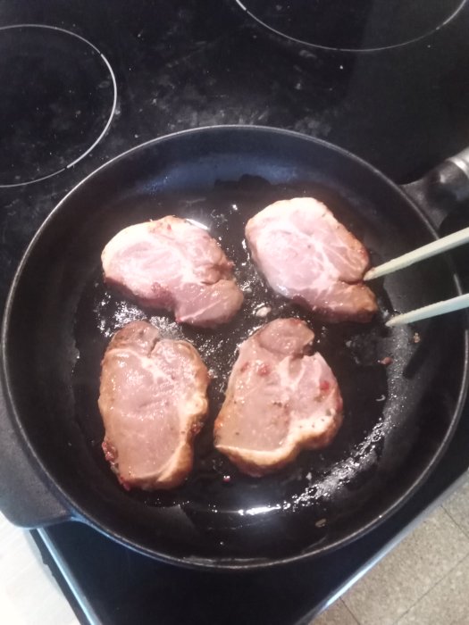 Fyra medaljonger av kött som steks i en svart stekpanna på en spishäll i kök.