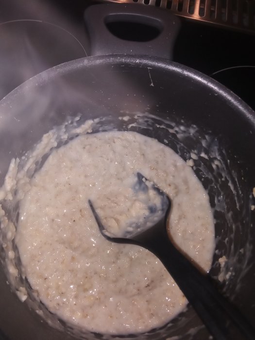 Havregrynsgröt kokad på komjölk i svart kastrull med slev.