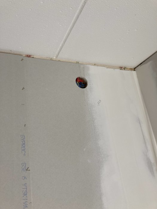 Gipsskiva asennettuna seinään; oikeassa yläkulmassa näkyy käyttämätön pistorasia, joka herättää kysymyksen peittämisestä sisustustapetilla.