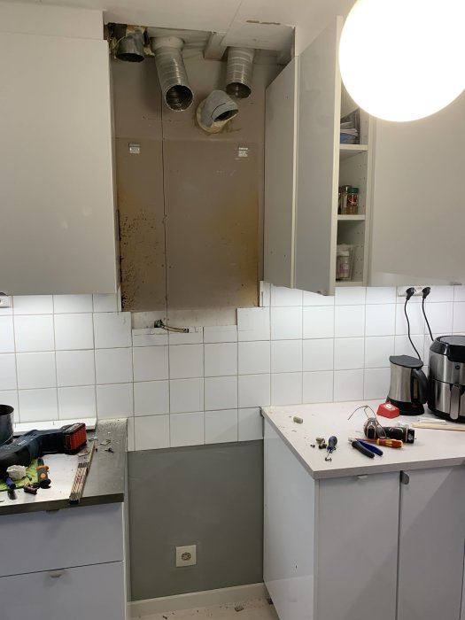 Kök under renovering med borttagen skåpssektion och synliga ventilationstrummor samt verktyg på arbetsyta.