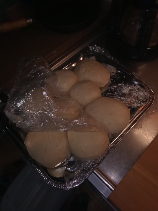 Oformade bullar i bakplåt förberedda för jäsning täckta med plastfolie.