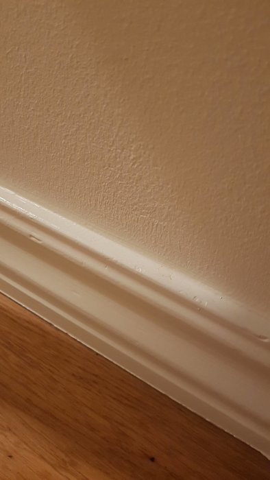 Vit golvlist mot beige vägg ovanför ett parkettgolv.