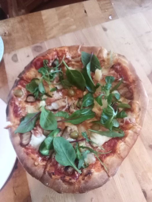 Hemlagad pizza med spenat och oliver på ett träbord.