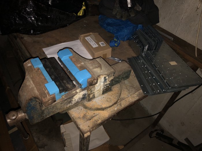 Vice on a workbench with larger perforated plates for homemade brackets, showing tools and materials in a workshop setting.