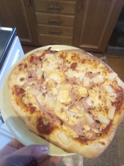 Hemlagad pizza med skinka och kiwi på ett köksbord.