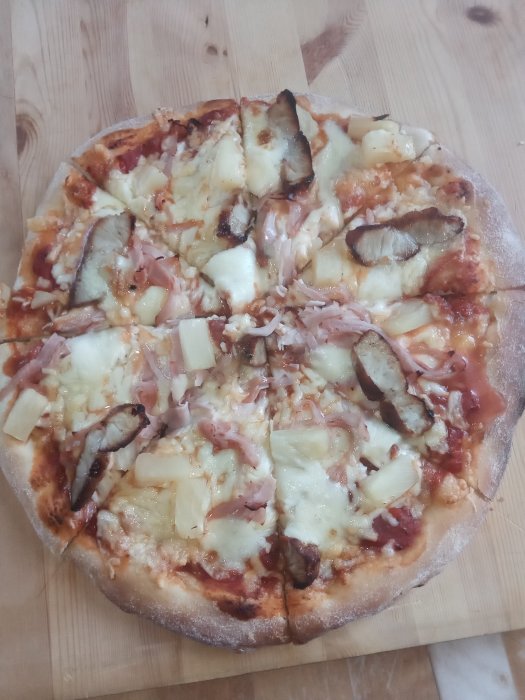 Hemlagad pizza med skinka, ananas och bruna kiwiskivor på en träskärbräda.