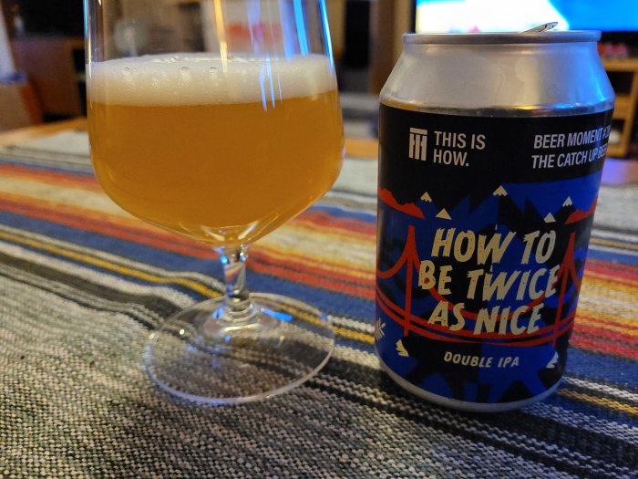 Ölglas med skummande IPA och en burk med texten "HOW TO BE TWICE AS NICE Double IPA" på ett färgglatt underlag.