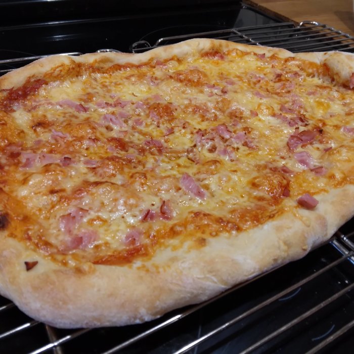 Hemlagad pizza med krispig botten, smält ost och skinka på ugnsgaller.
