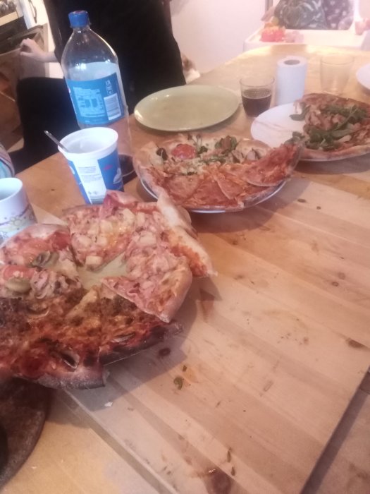 Resterna av nio olika pizzor på ett träbord med tomma dryckesbehållare.