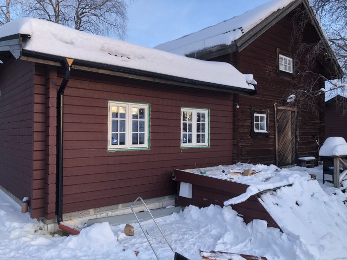 Nyinstallerade fönster på en röd träfasad med snö på marken och takkanten.