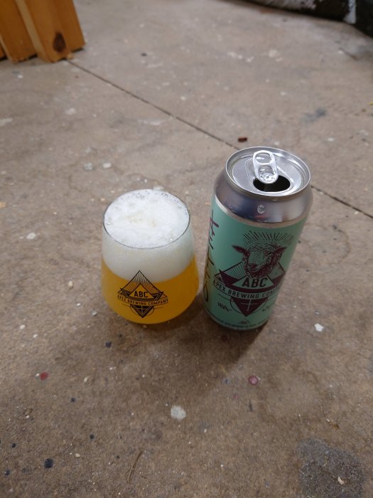Öppnad burk av Apex IPA och ett glas fyllt av skummande öl på en betongyta.
