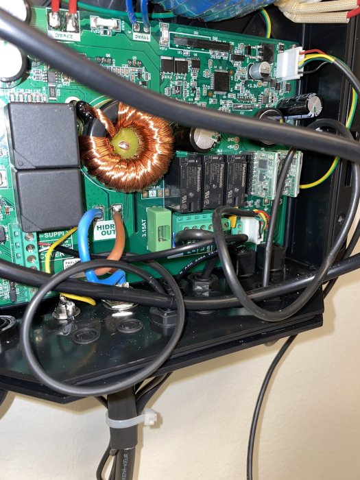 Inre komponenter och kretskort i en klorinator med kablar och en spole.