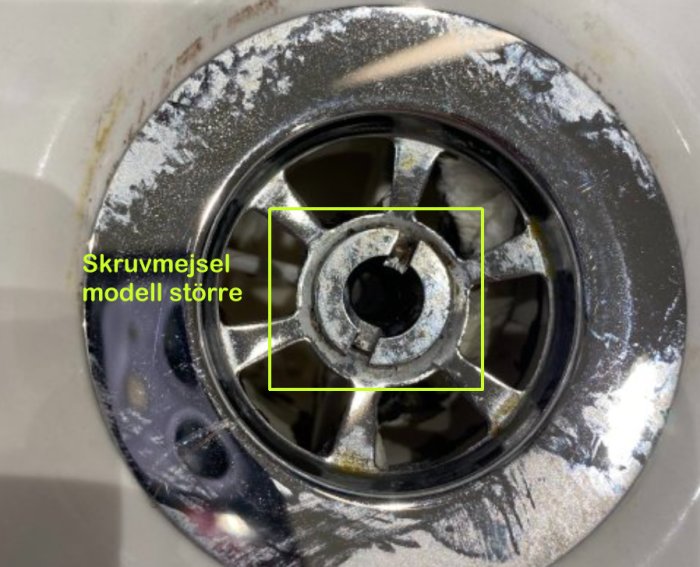 Närbild på en sliten avloppssil i handfat med en markerad skruv som kräver en stor skruvmejsel.