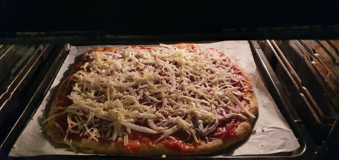 Hemlagad pizza med tomatsås och ost på bakplåtspapper i en ugn.