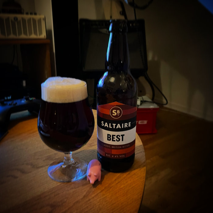 Flaska och glas av Saltaire Best bitteröl på ett bord, med musikutrustning i bakgrunden.