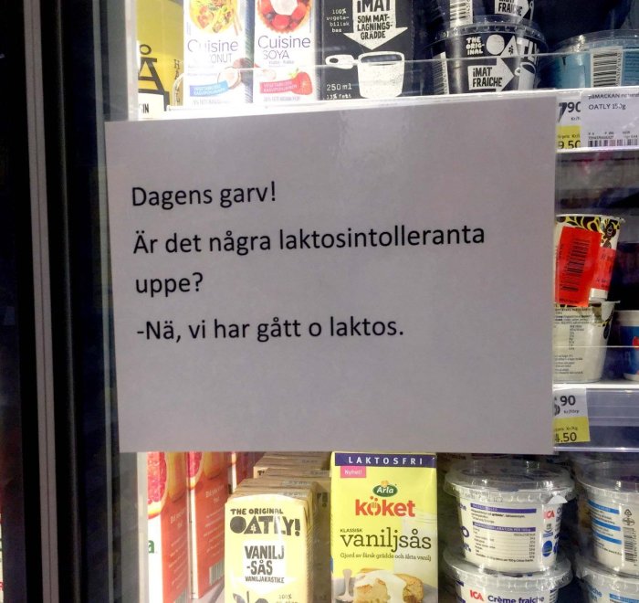 Skämt på skylt om laktosintolerans framför hylla med laktosfria produkter i en butik.