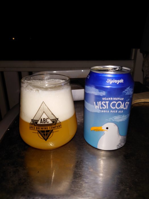 Ölglas fullt av skum och Stigbergets ölburk på bord i skymningen.