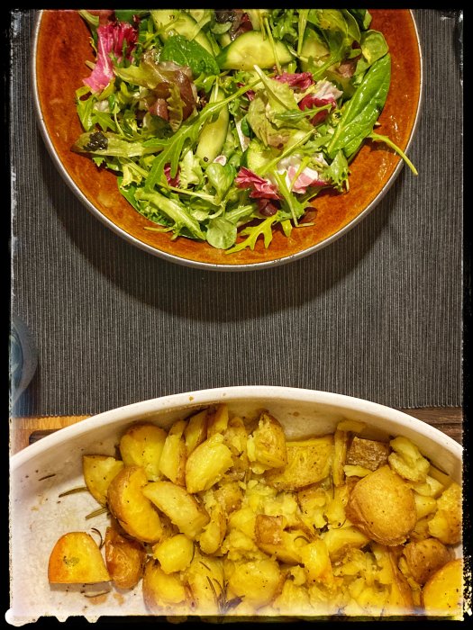 En skål med blandad grönsallad och en form med rostade potatisar, tillbehör till en kötträtt.
