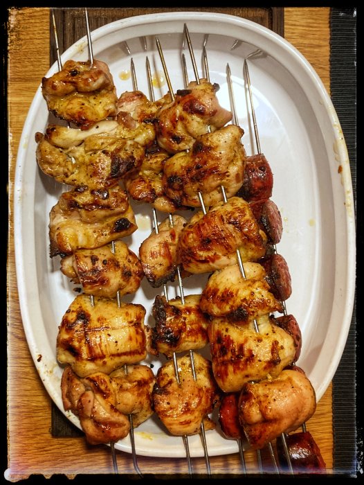 Grillade spett med kyckling och korv på en vit tallrik.
