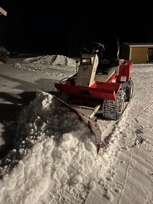 En 23 år gammal röd och vit snöplog i arbete på natten, med synliga snöspår och upplyst av strålkastare.