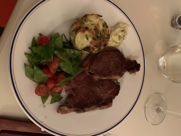Måltid med lokalproducerad biff, potatisbakelse och sallad på en tallrik, bredvid ett glas vin.