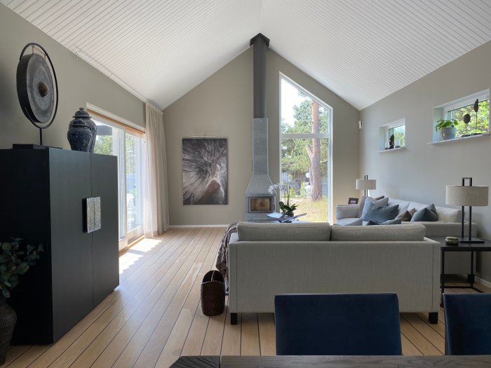 Vardagsrum med vitt ryggåstak och väggar som möter taket, grå soffa och öppen spis.