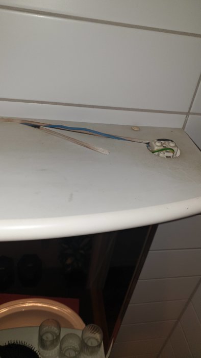 Eluttag utan frontplatta på en smutsig vit arbetsyta med synliga elektriska ledningar.