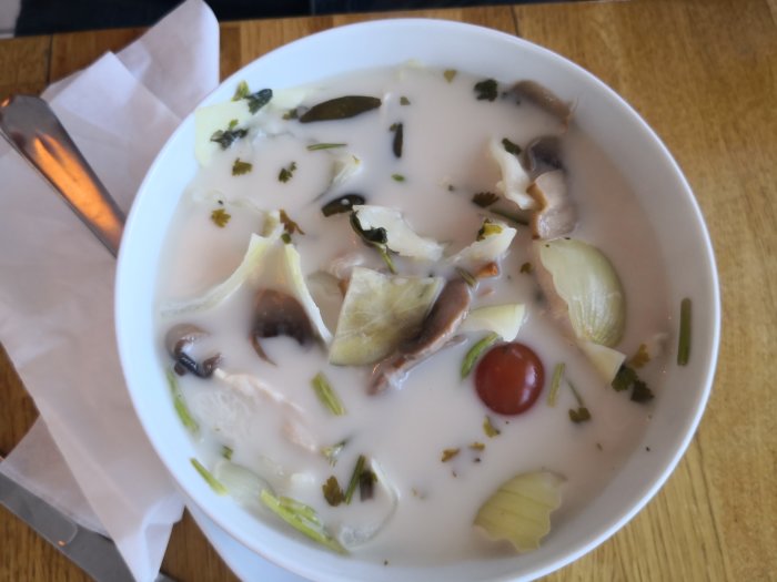 En skål med thailändsk soppa med grönsaker och svamp på ett träbord.