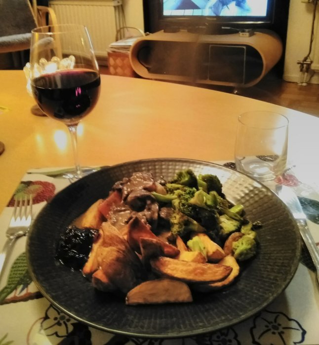 Middagstillagning med kronhjortsgryta, rotfrukter, stekt broccoli och potatisklyftor på tallrik, med ett glas rött vin.