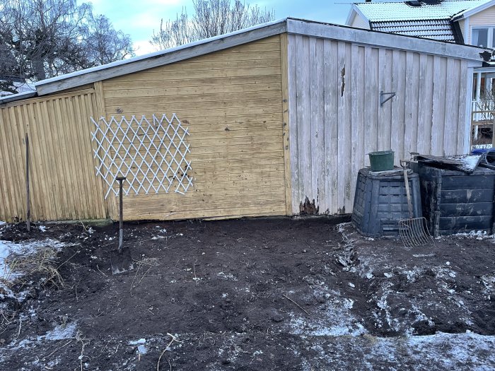 Nygrävd mark bredvid ett vedskjul med spade, kompostbehållare och snörester.