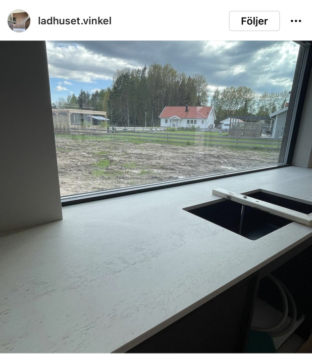 Köksbänk med integrerad spishäll nära ett stort fönster med utsikt över en lantlig tomt.