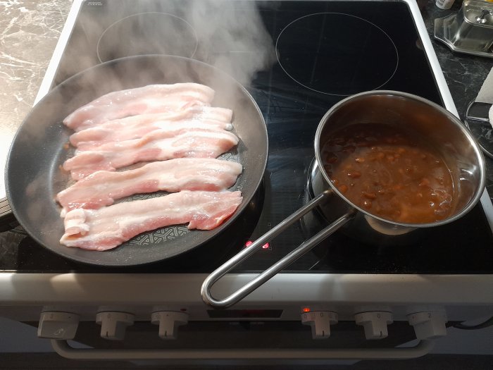 Stekande bacon i panna och bönor i tomatsås i kastrull på spis.