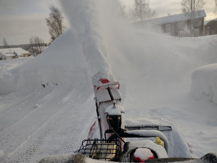 Snöslunga i arbete som kastar iväg snö på en solig dag med snötäckta omgivningar.