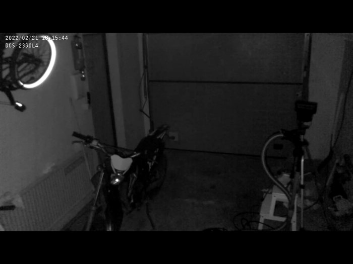 Svartvit övervakningsbild av ett garage i totalt mörker med ir-ljus, synliga cyklar och en stängd port.